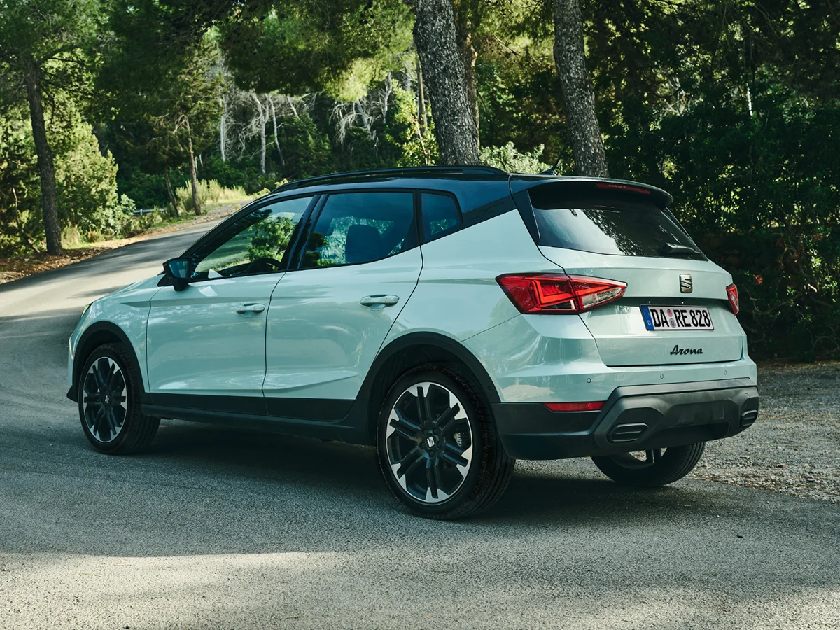 SEAT Arona in der Farbe Oniric Lake vor grünem Glasgebäude auf leerem Parkplatz